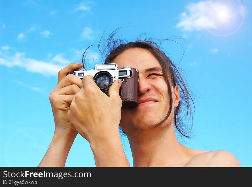 Young man holding old camera, focusing the image, against blue sky. Young man holding old camera, focusing the image, against blue sky