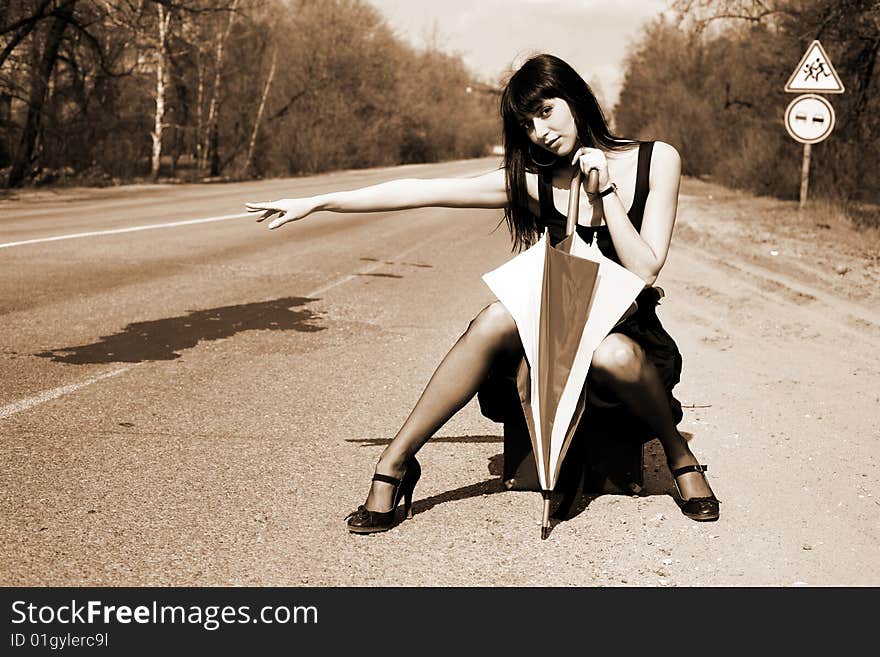 Girl in the road sit atop vintage suitcase with umbrella