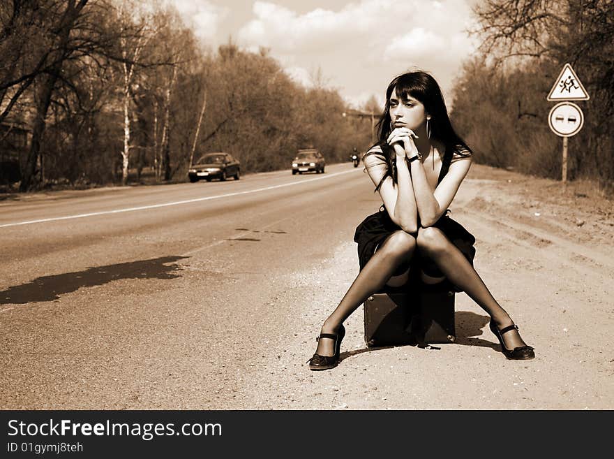 Girl in the road sit atop vintage suitcase