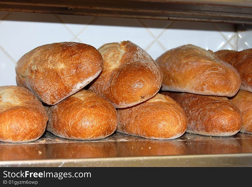 This is a shot of some bread loaves on a stainless steel shelf ready to be cut and served.