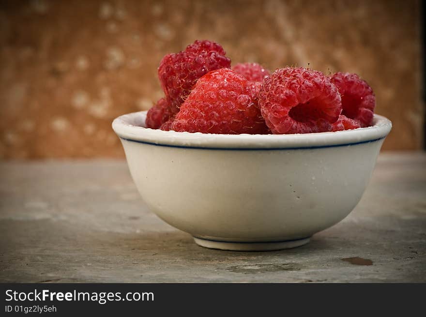 Ripe raspberries in small bowl on slate background.