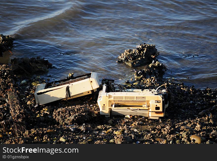 Discarded printer rusting on the ocean shore amongst clams and rocks causing pollution. Discarded printer rusting on the ocean shore amongst clams and rocks causing pollution.