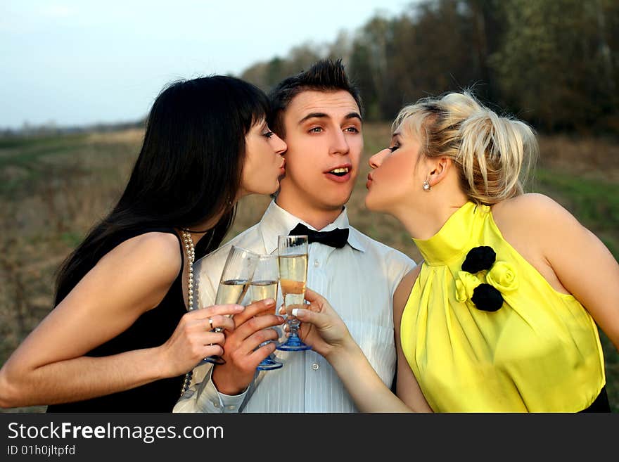 Two girl with wine kissing man outdoors. Two girl with wine kissing man outdoors