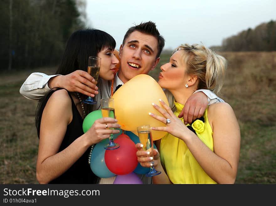 Two girl with wine kissing man outdoors. Two girl with wine kissing man outdoors