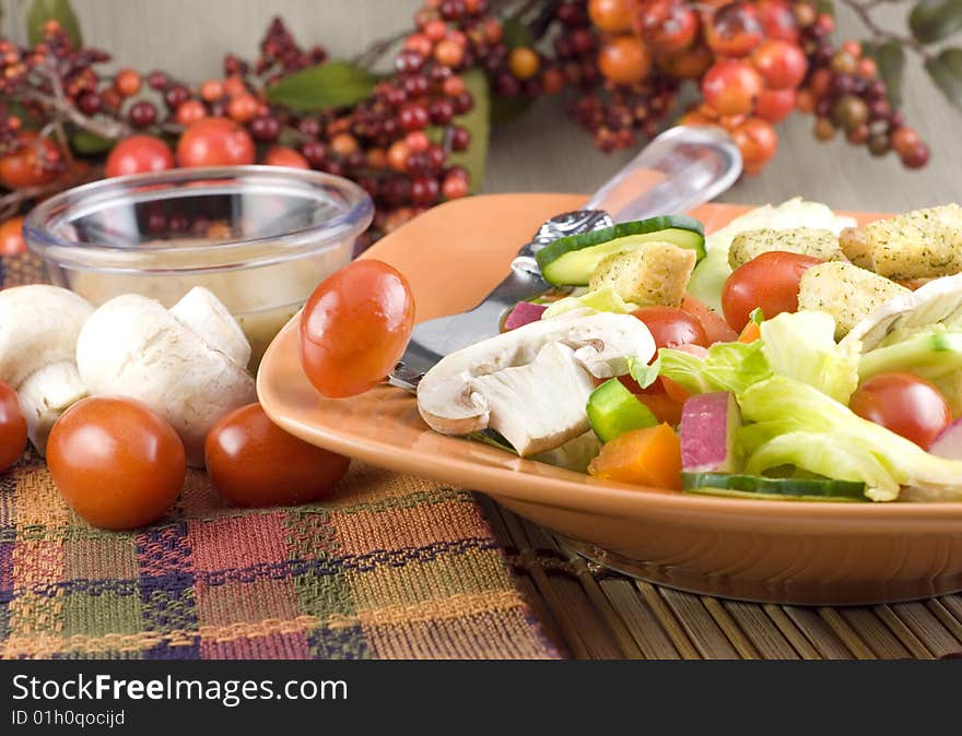 Colorful garden salad with mushrooms, tomatoes, and Italian dressing in orange bowl with fall colored table setting copy space