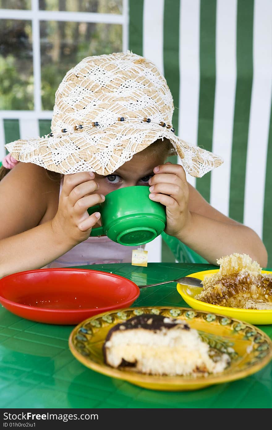 Little girl in big hat eats sweets and drinks tea