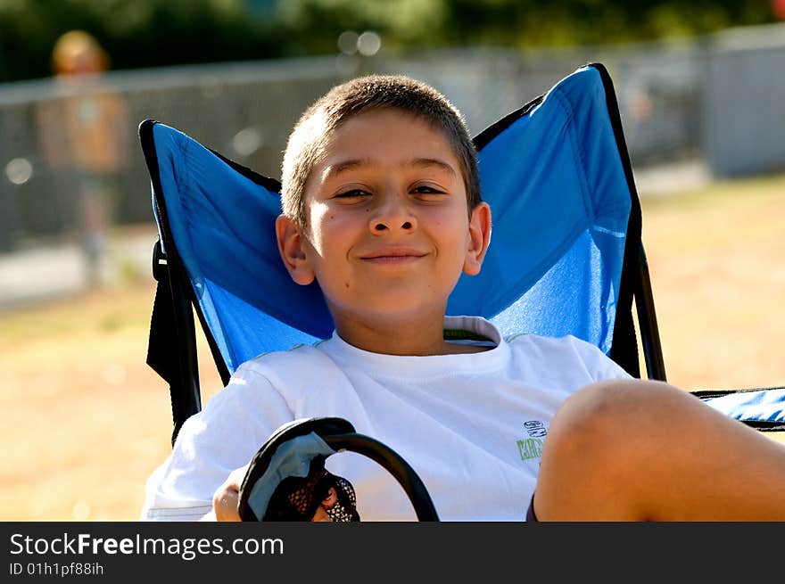 A young boy sitting in a blue chair on a public playground. A young boy sitting in a blue chair on a public playground