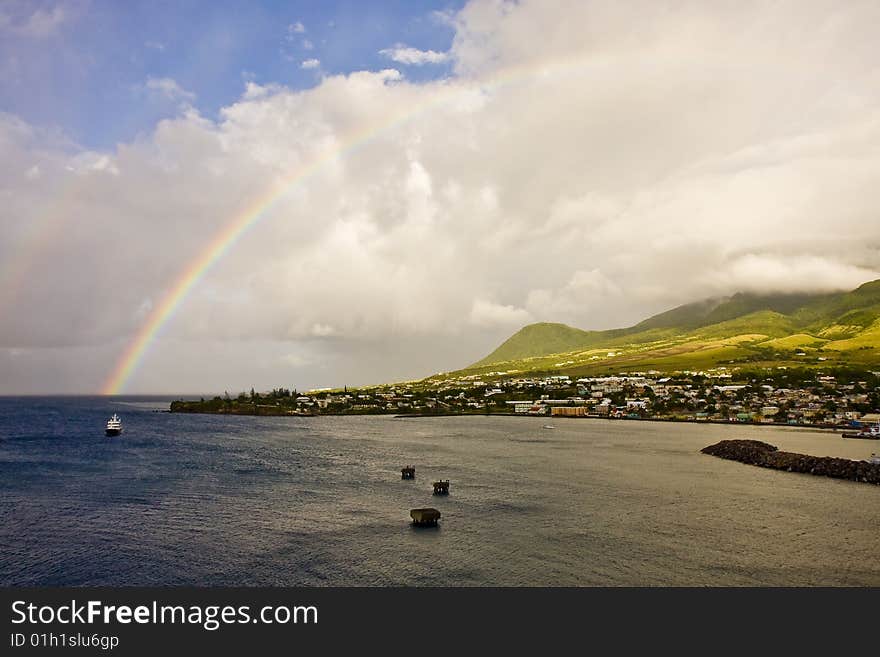 A rainbow in the morning clouds off of a lush green island