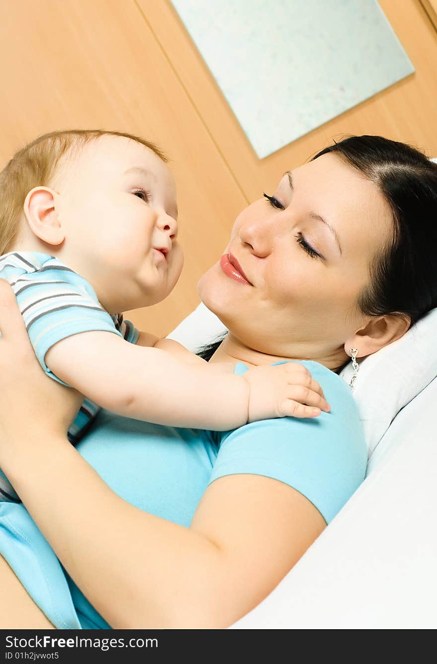 Young mother lies on the bed with her ten months old baby. Young mother lies on the bed with her ten months old baby