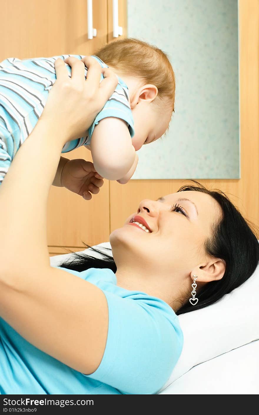 Young brunette mother lies on the bed with her ten months old baby. Young brunette mother lies on the bed with her ten months old baby