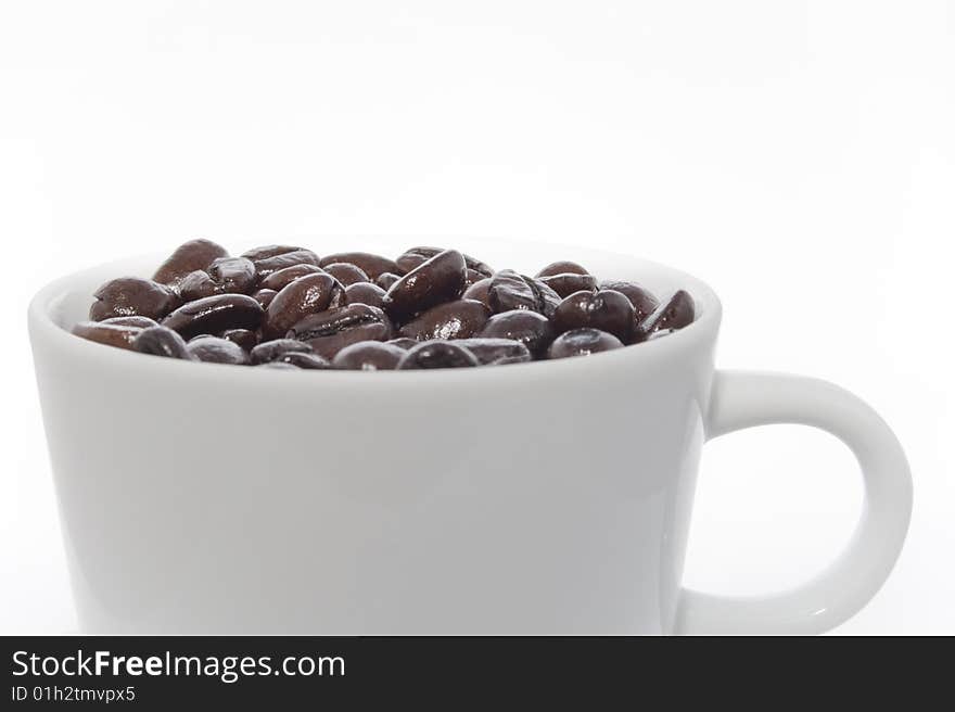 Frontal view of a white cup of coffee beans. Light from above left; reflection in beans.