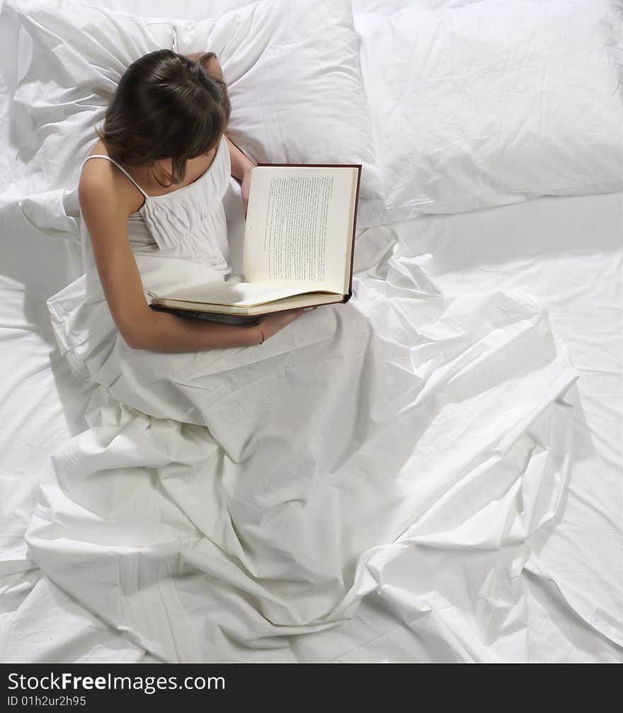 A pretty young woman reads a book in bed