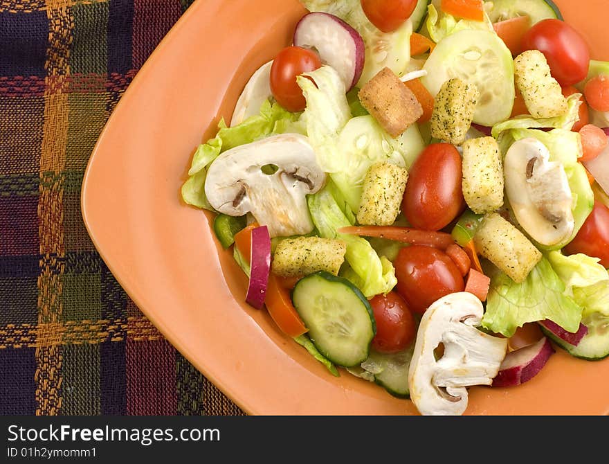 A closeup image of a fresh garden salad with mushrooms in orange bowl on a plaid fall colored mat  copy space. A closeup image of a fresh garden salad with mushrooms in orange bowl on a plaid fall colored mat  copy space