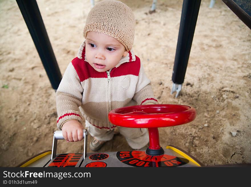 A young child playing with a driving toy on a playground. . A young child playing with a driving toy on a playground.