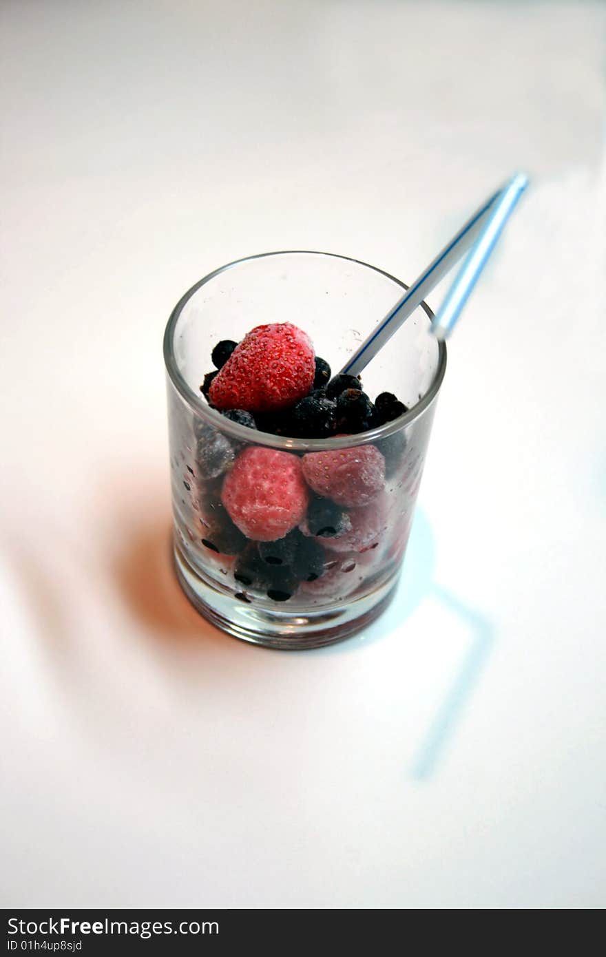 Frozen berries in glass with tube for a cocktail; frozen strawberry and currant;
 Fresh cocktail from berries