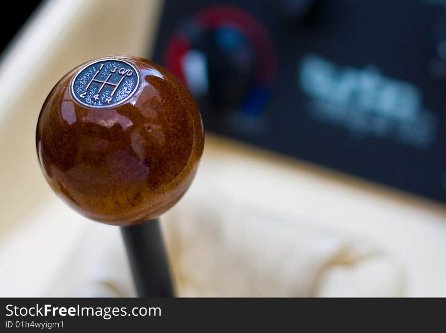 A polished wooden gear knob within a sports car, against the background of the dials of the centre console and leather of the upholstery. A polished wooden gear knob within a sports car, against the background of the dials of the centre console and leather of the upholstery