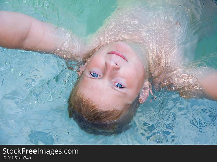 Handsome caucasian boy in pool laying back in pool looking at camera,smiling,blue eyes,blond hair. Handsome caucasian boy in pool laying back in pool looking at camera,smiling,blue eyes,blond hair