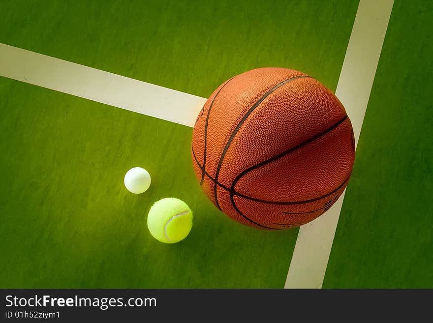 A basketball, a tennis ball and a Ping-Pong ball on the green background