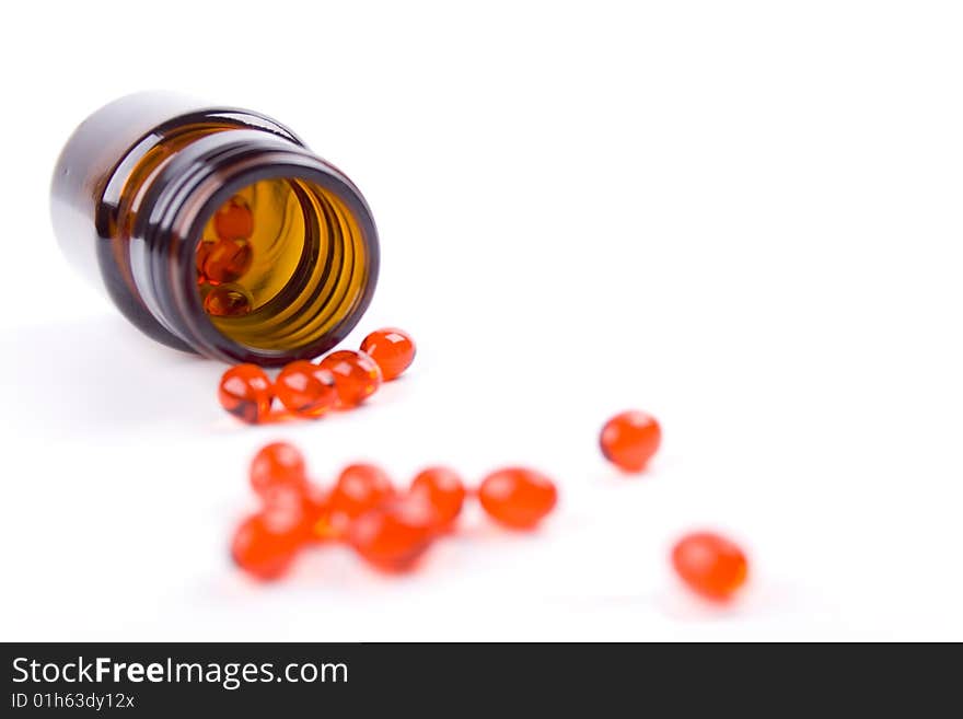 Glass bottle with red pills on white background