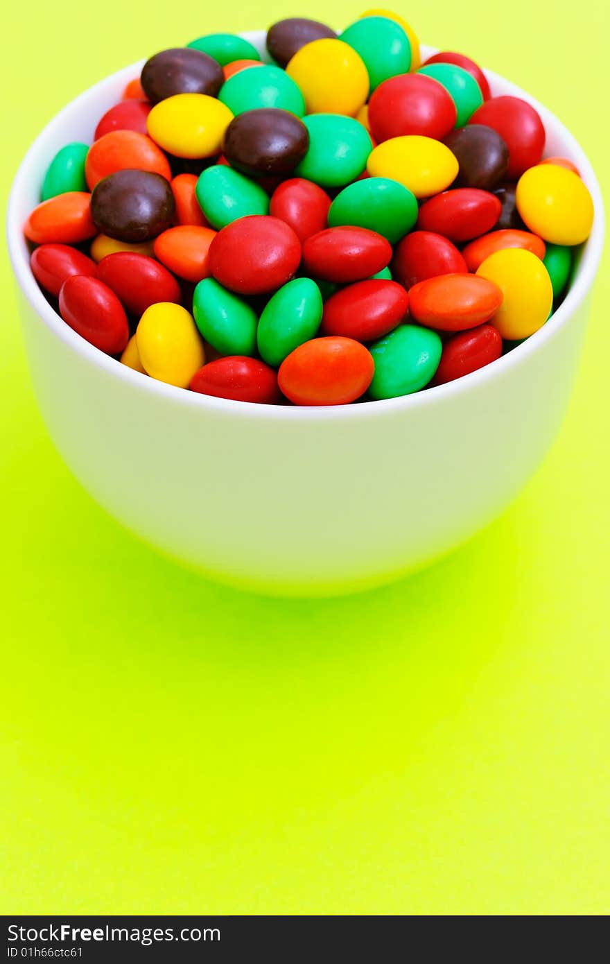 White bowl full of candies on lettuce green background with copy space. White bowl full of candies on lettuce green background with copy space.