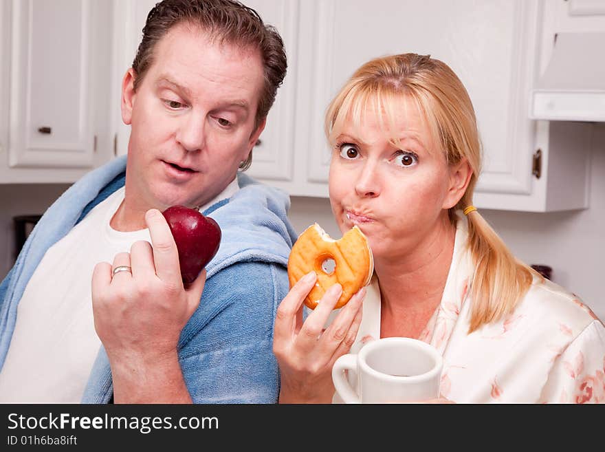 Couple in Kitchen Eating Donut and Coffee or Healthy Fruit. Couple in Kitchen Eating Donut and Coffee or Healthy Fruit.