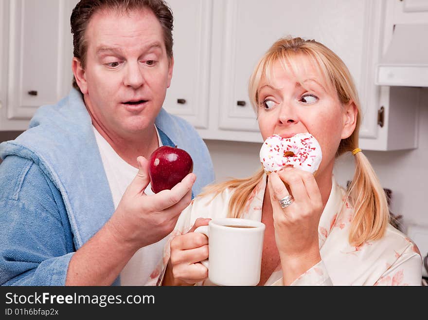 Couple in Kitchen Eating Donut and Coffee or Healthy Fruit. Couple in Kitchen Eating Donut and Coffee or Healthy Fruit.