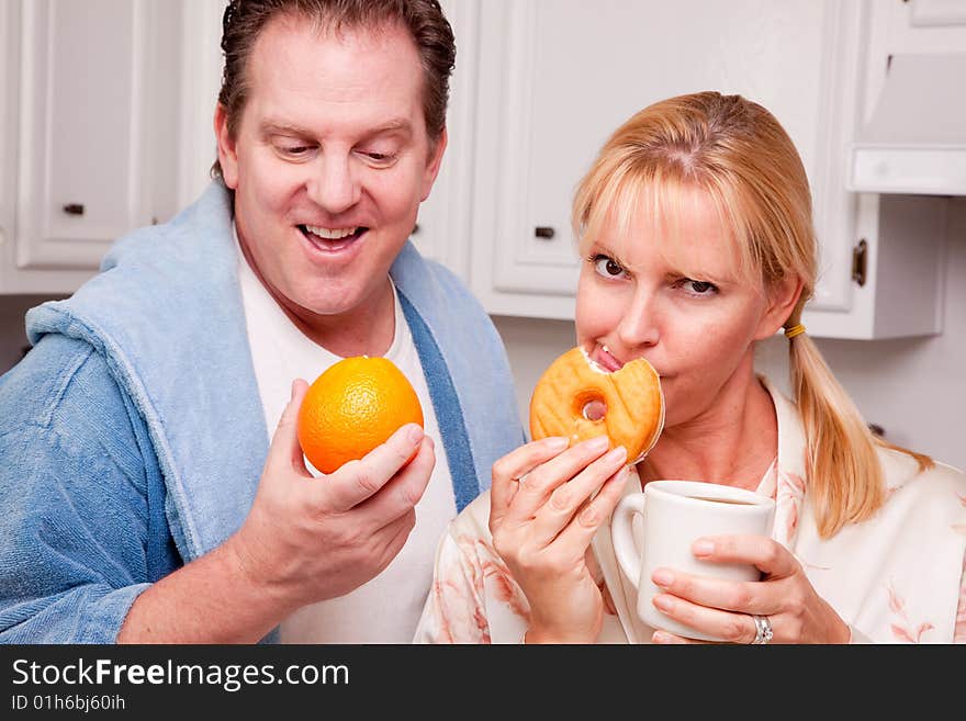 Couple in Kitchen Eating Donut and Coffee or Healthy Fruit. Couple in Kitchen Eating Donut and Coffee or Healthy Fruit.