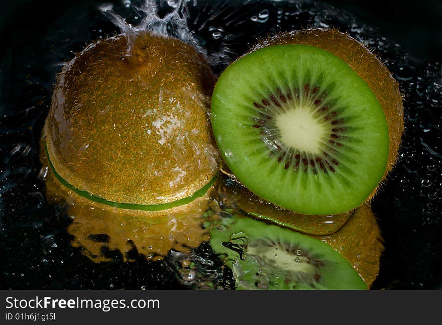 Kiwi dousing with water, with reflection, on black background