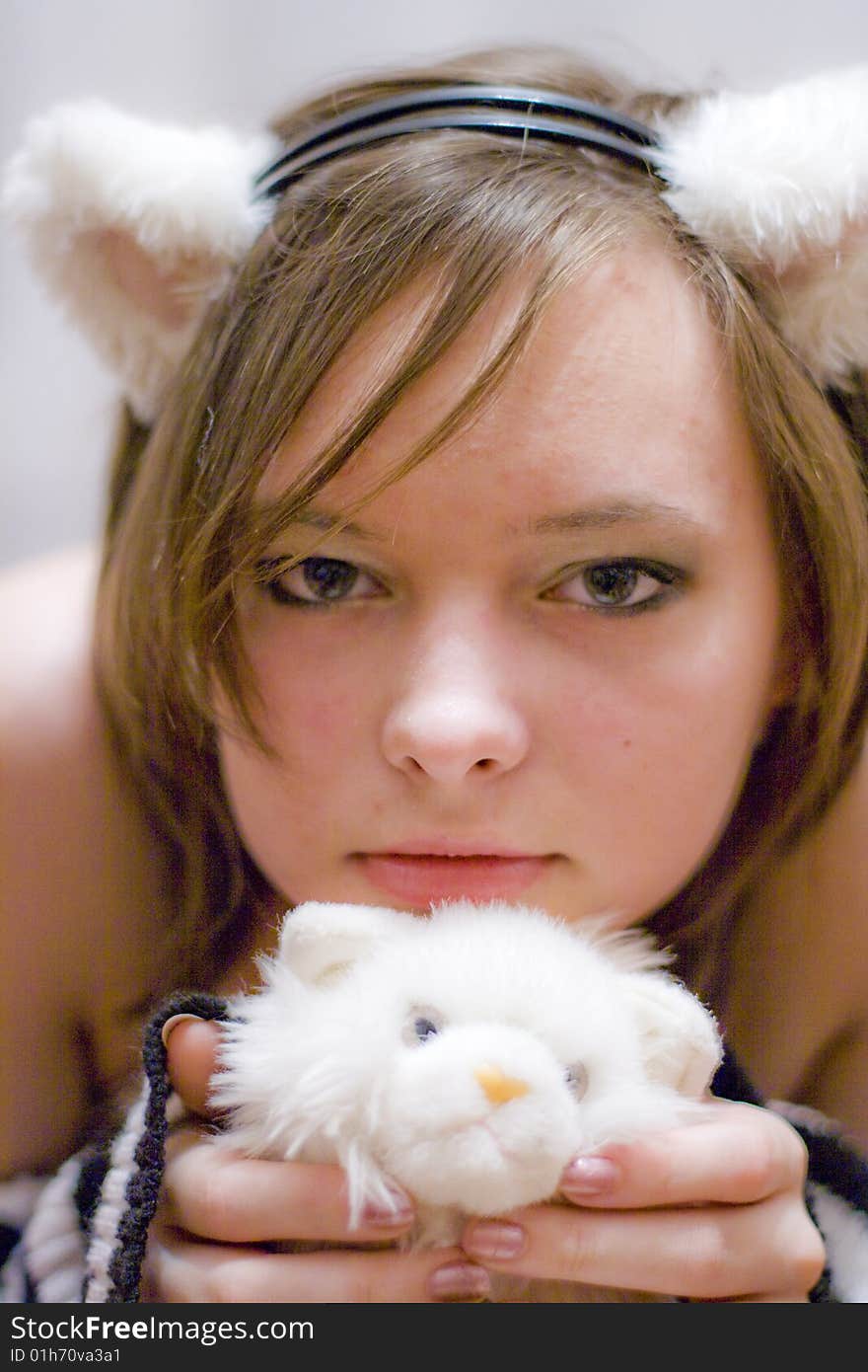 Sweet girl with the ears on your head. Beautiful girl holds a toy - white kitten. Sweet girl with the ears on your head. Beautiful girl holds a toy - white kitten