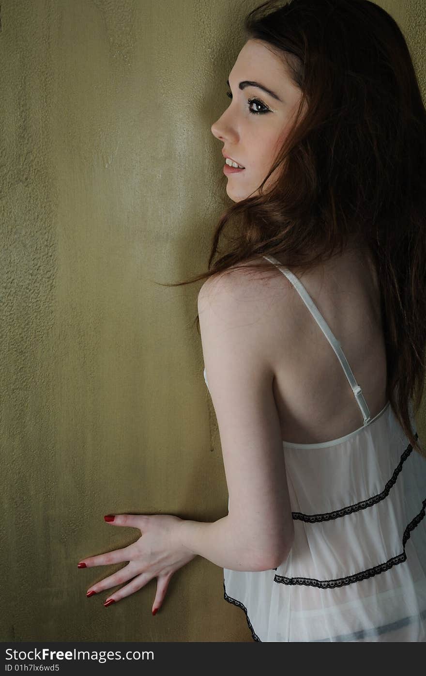 Female model looking over her shoulder to the left wearing see through matching lingerie set and painted nails on a golden background. Female model looking over her shoulder to the left wearing see through matching lingerie set and painted nails on a golden background