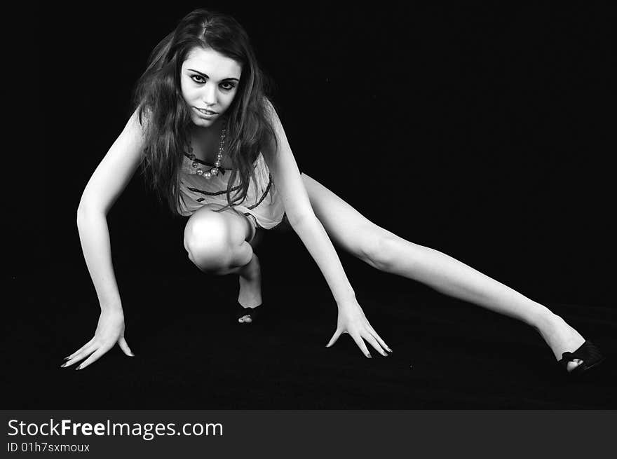 Female model stretching one leg out to her left balancing on one foot and her finger tips against a black background. Black and white image. Female model stretching one leg out to her left balancing on one foot and her finger tips against a black background. Black and white image