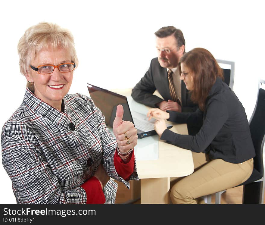 Businesswoman showing tumb up sign in office environment. Three people with focus on mature woman in front. Isolated over white. Businesswoman showing tumb up sign in office environment. Three people with focus on mature woman in front. Isolated over white.