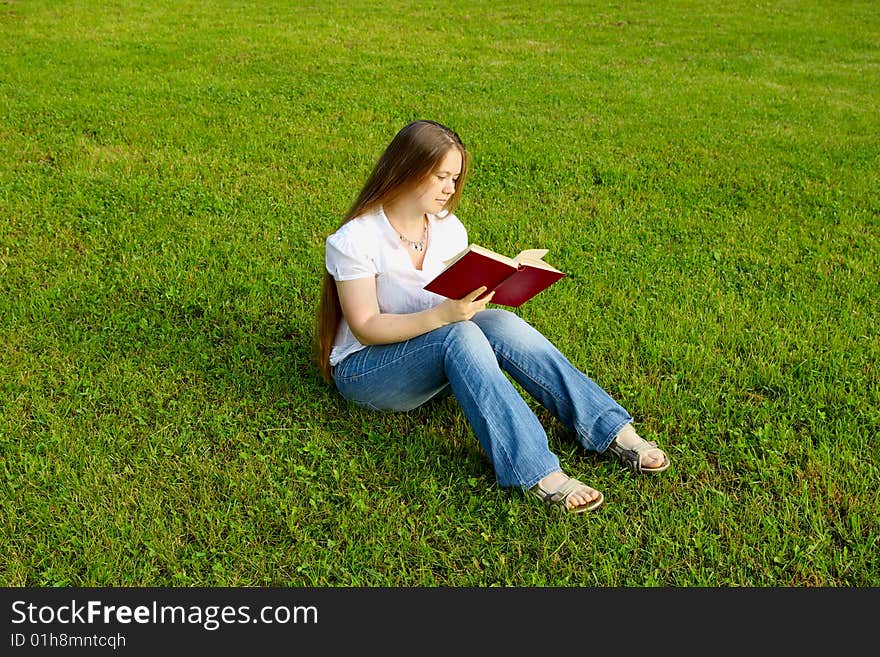 Blond girl reading red book over the grass. Blond girl reading red book over the grass