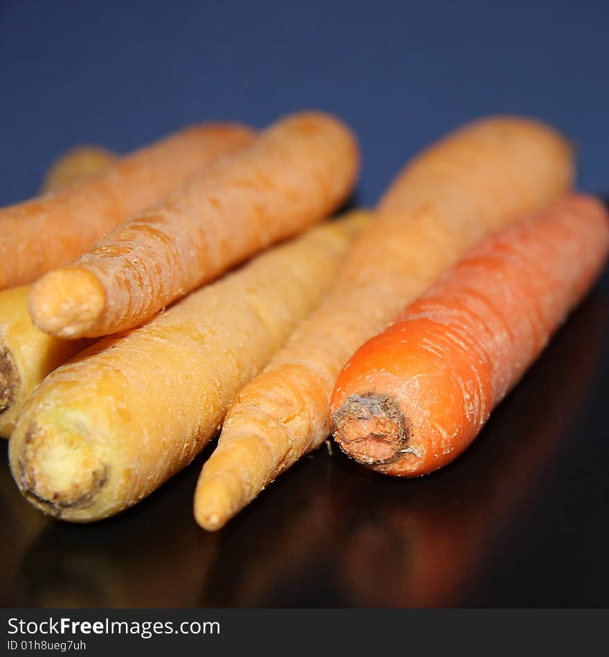 White, light orange, and deep orange raw carrots set against a blue background and on a black surface. White, light orange, and deep orange raw carrots set against a blue background and on a black surface.