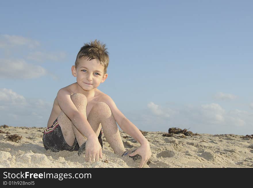 A cute young boy enjoys squishing his toes in the sand. A cute young boy enjoys squishing his toes in the sand.