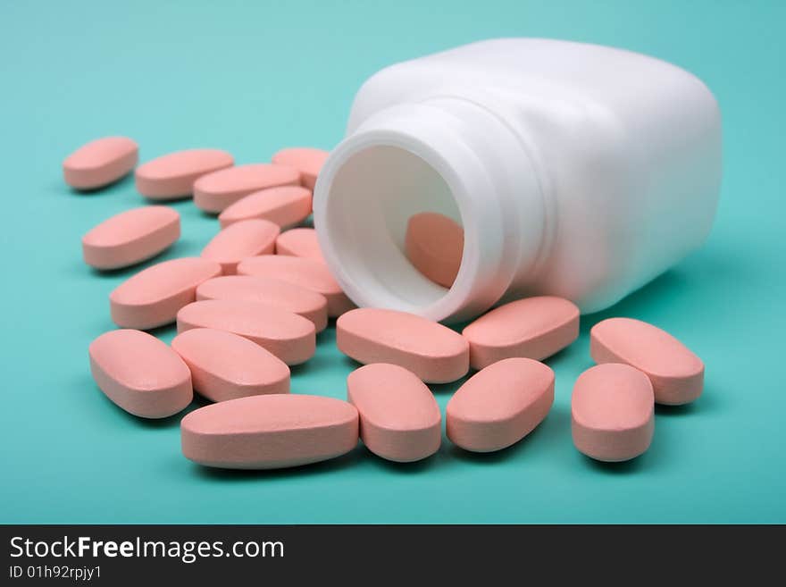 Close-up of pills scattered around the white bottle on a green background. Close-up of pills scattered around the white bottle on a green background