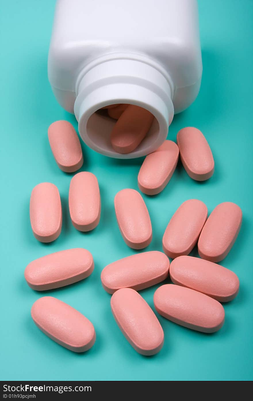 Close-up of pills scattered around the white bottle on a green background. Close-up of pills scattered around the white bottle on a green background