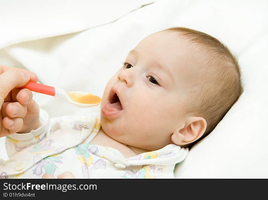 Hand of mother feeds the baby lying on a white bed-sheet. Hand of mother feeds the baby lying on a white bed-sheet.