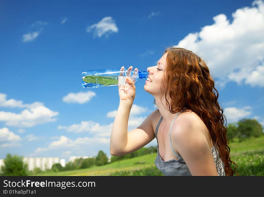 The woman in a profile drinks water from a bottle in park. The woman in a profile drinks water from a bottle in park