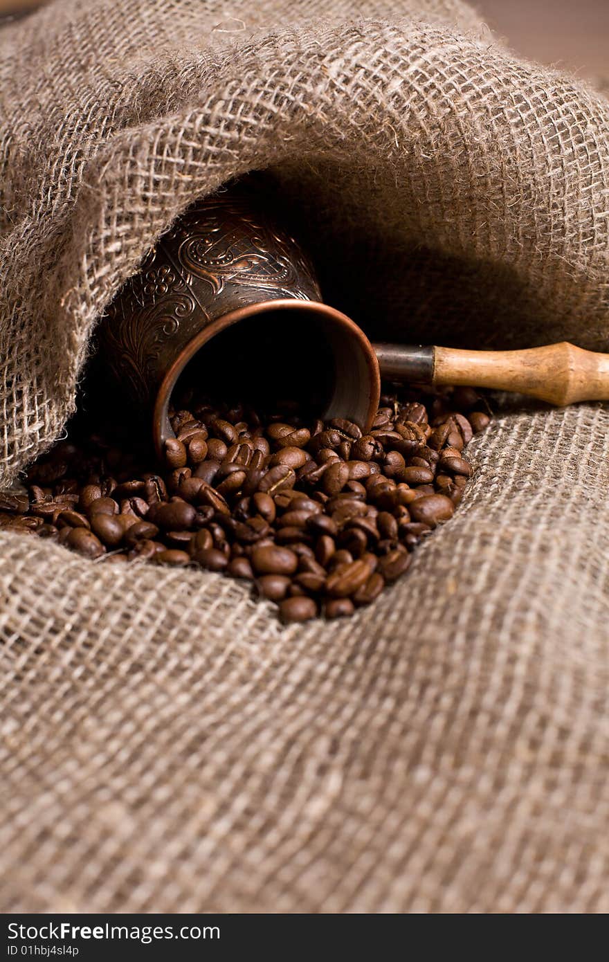 Cezve with freshly roasted coffee beans on sackcloth. Shallow depth of field. Focus on center of image