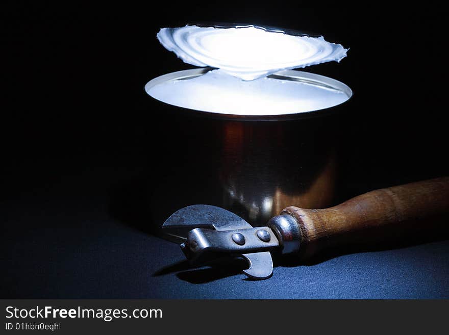 Can opener lying near opened tin with glow inside. Can opener lying near opened tin with glow inside