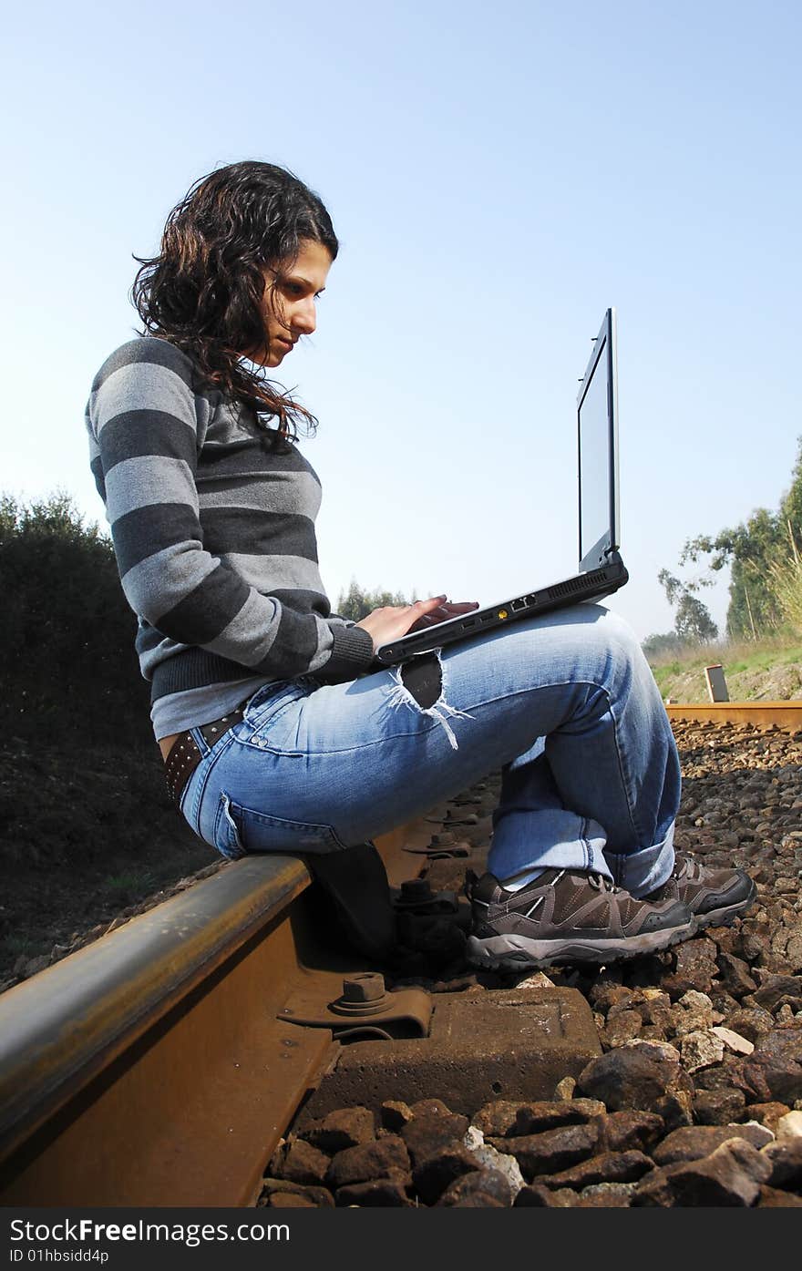 Pretty girl waiting for the train on a railway with a laptop, computer