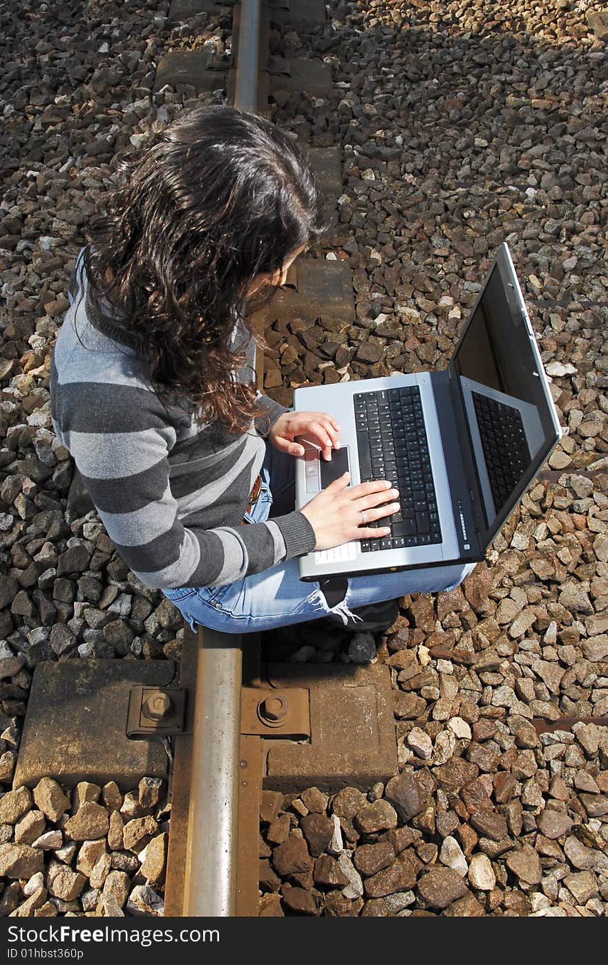 Pretty girl waiting for the train on a railway with a laptop, computer