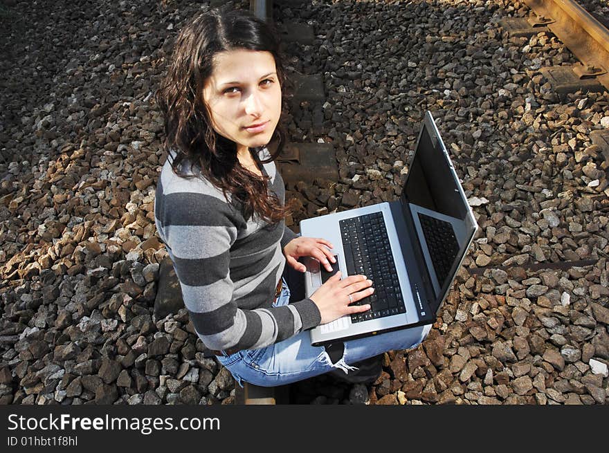 Pretty girl waiting for the train on a railway with a laptop, computer