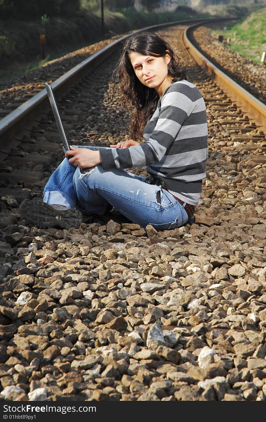 Pretty girl waiting for the train on a railway with a laptop, computer