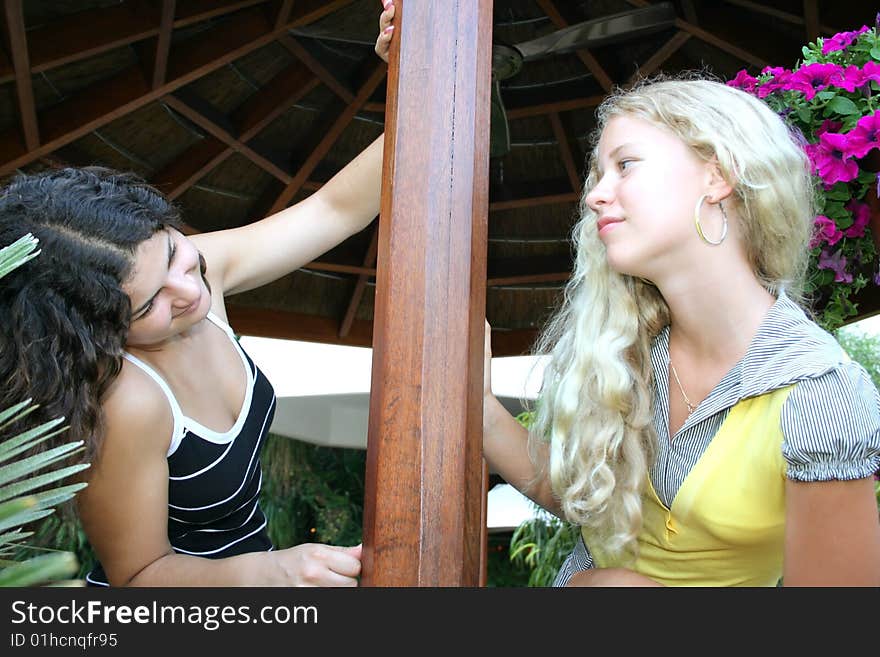 Pretty brunette and blond girls on veranda in tropics.