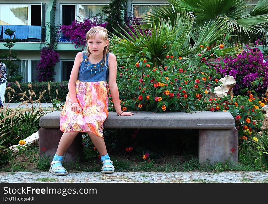 Sad girl sitting on bench in flower bed