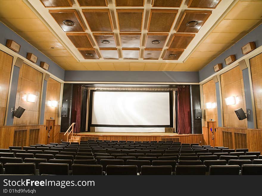 Empty old retro style cinema auditorium with line of chairs and stage with silver screen. Ready for adding your own picture. Empty old retro style cinema auditorium with line of chairs and stage with silver screen. Ready for adding your own picture.