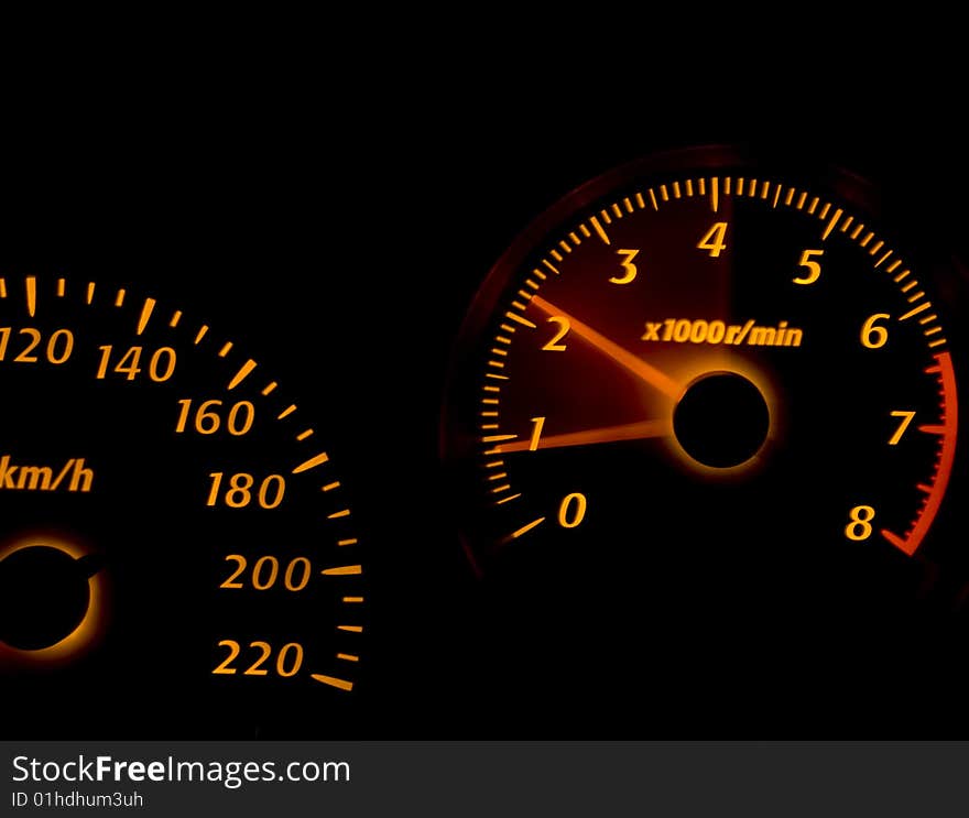 Car dashboard gauges illuminated at night, tachometer, speedometer