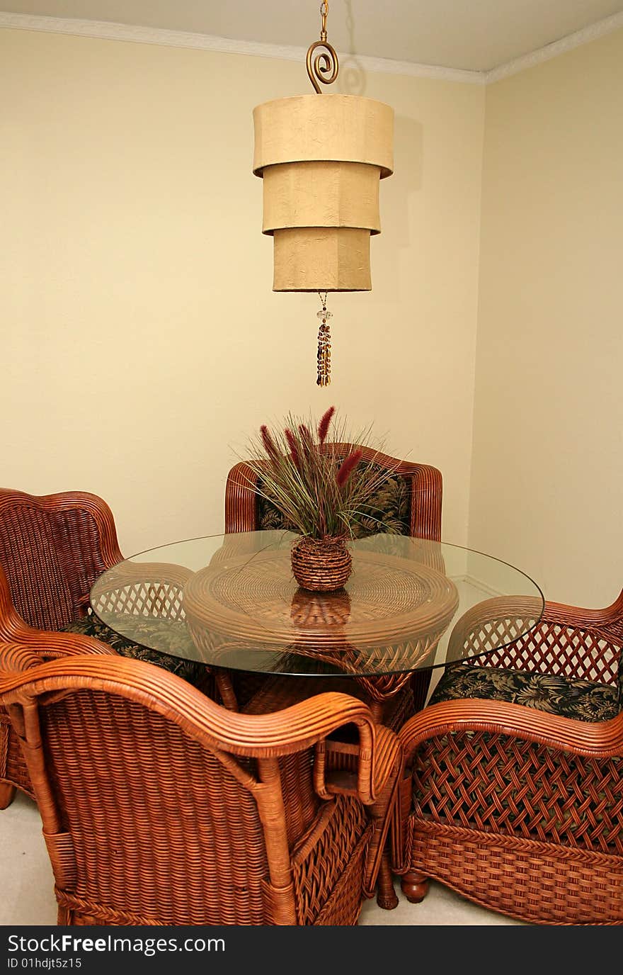 A dining room is decorated with whicker furniture and a unique light fixture.